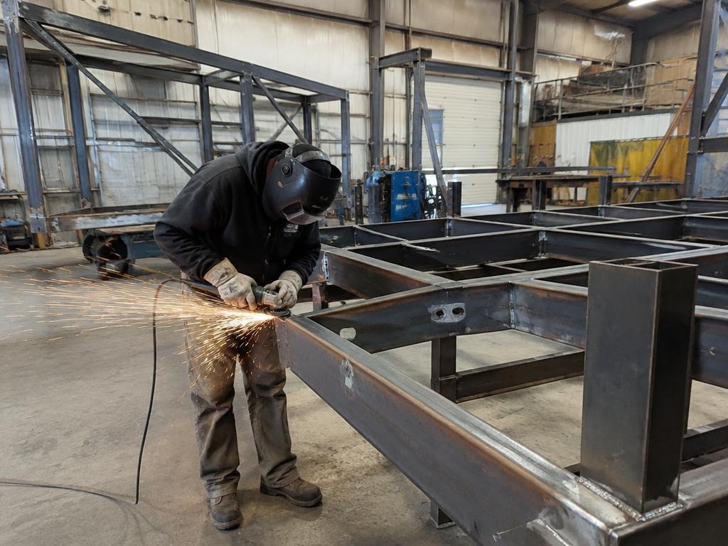 Welder grinding a fabricated steel frame in a workshop